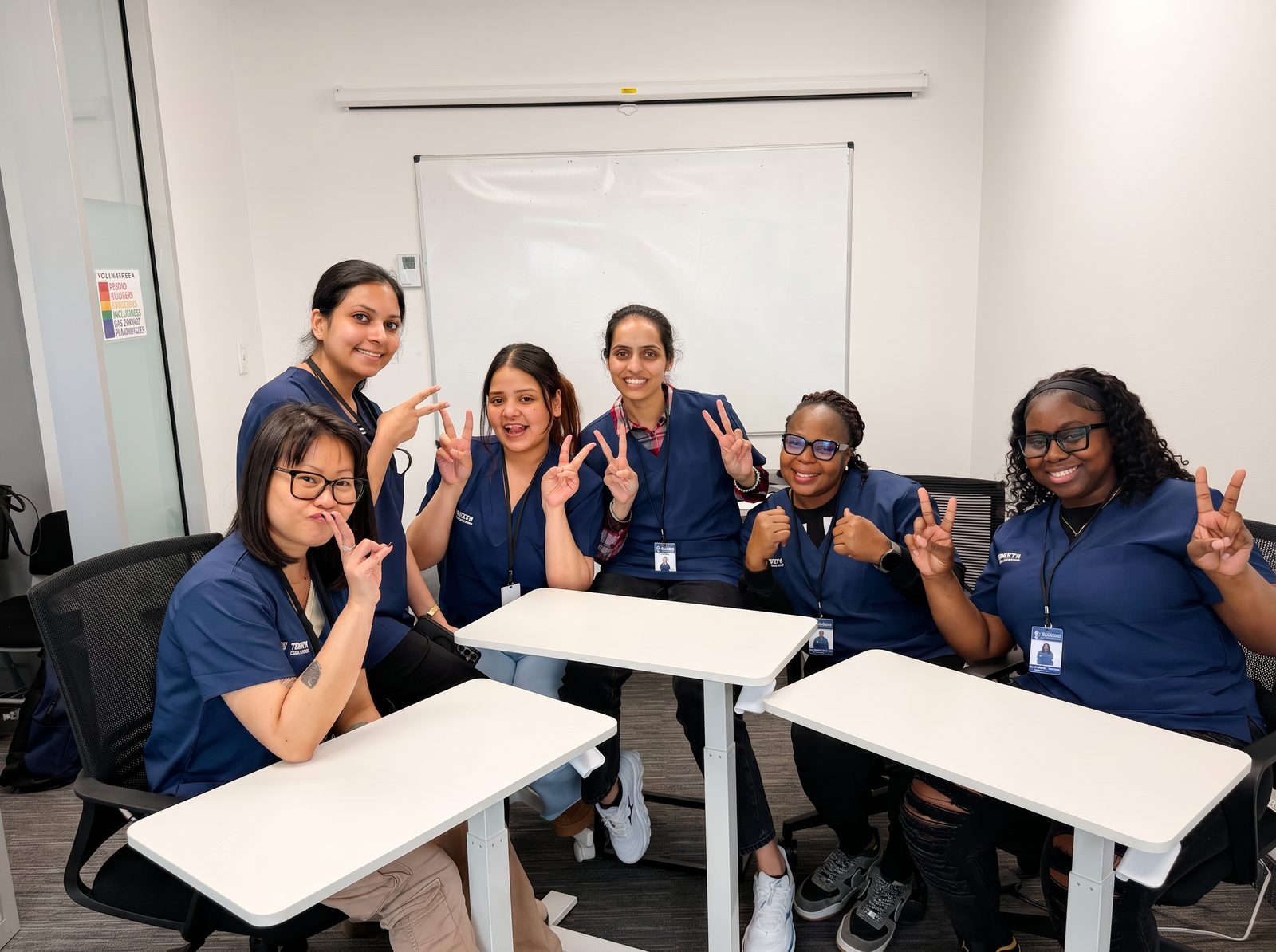 A diverse group of TAE PSW students in navy scrubs smiling together in a bright classroom